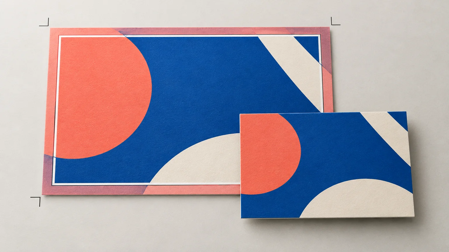 Editorial illustration of a colorful print layout with a pink bleed area and crop marks around a larger sheet, alongside a smaller trimmed card showing the final blue, coral, and cream design.